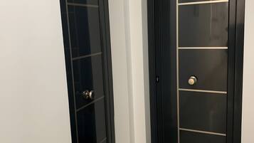Two black doors with glass panels and a metal handle, set in a hallway with a marble floor and a doormat.