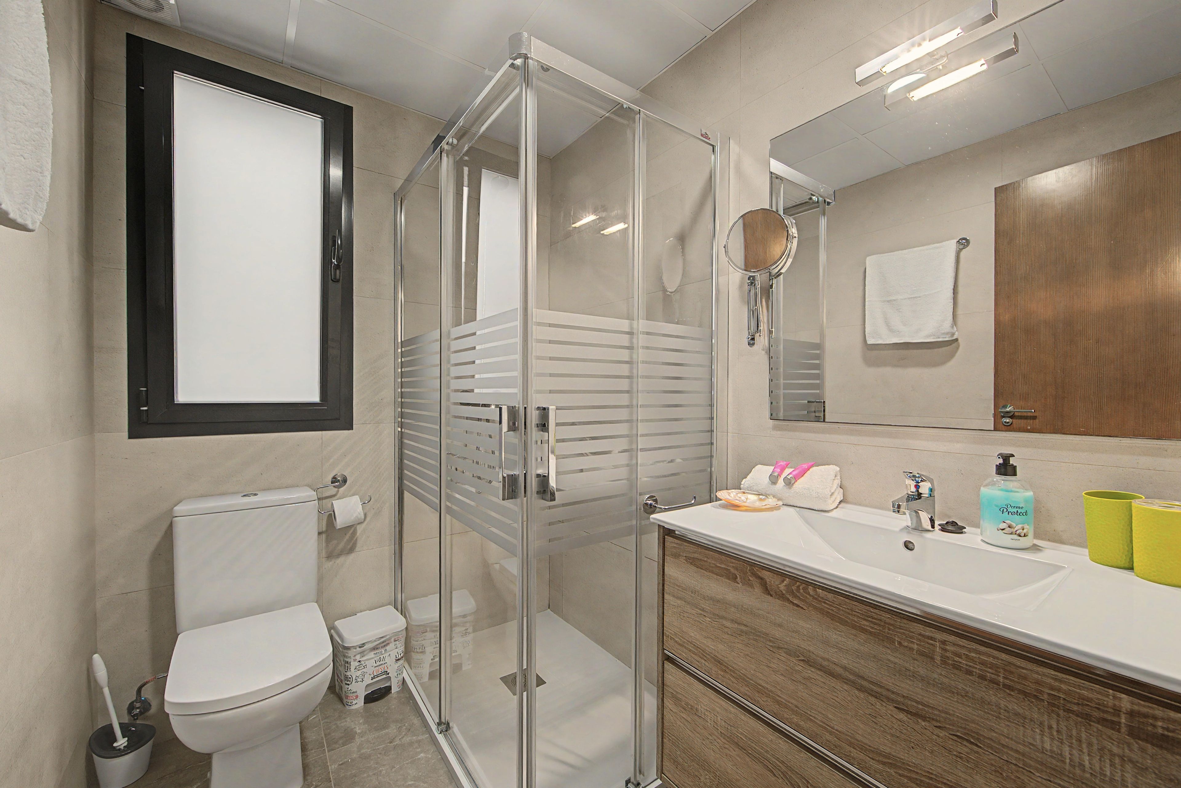 Een moderne badkamer met een douchecabine van glas, een toilet, een wastafel met toiletartikelen en een spiegel.