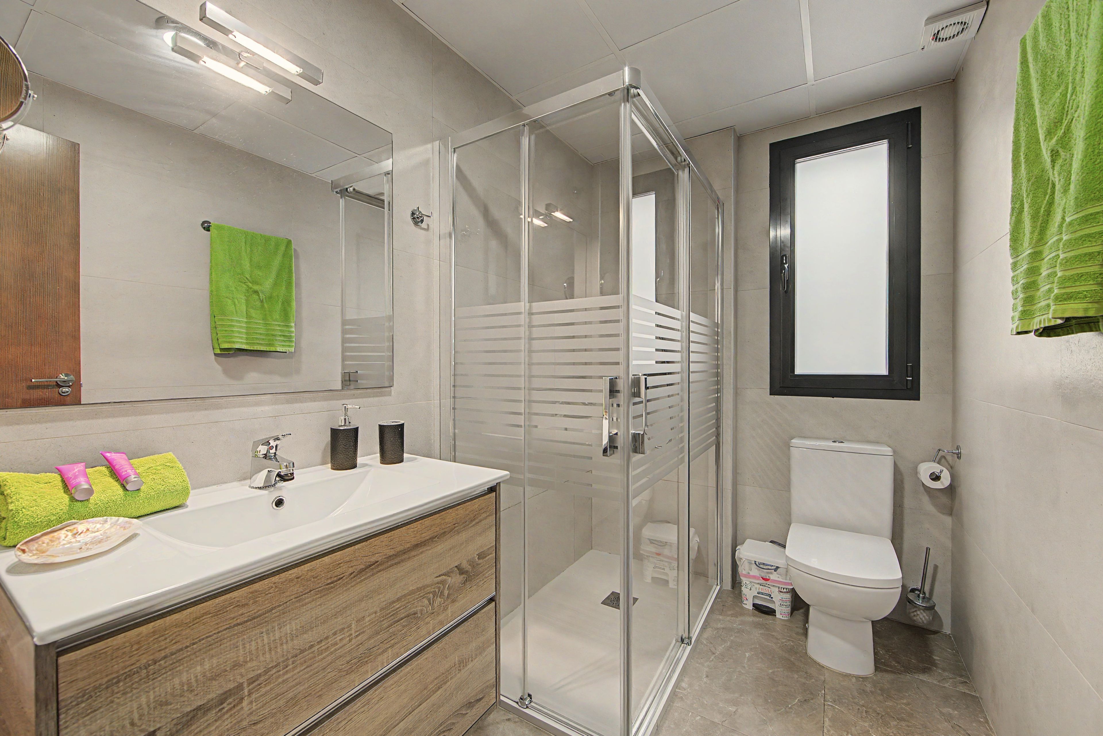 Een moderne badkamer met een glazen douchecabine, een witte wastafel met een houten kastje en een toilet.