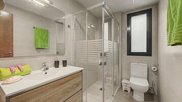 Een moderne badkamer met een glazen douchecabine, een witte wastafel met een houten kastje en een toilet.