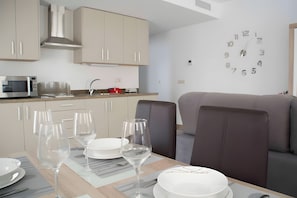 Een moderne keuken met een eethoek, een magnetron, een spoelbak en een klok aan de muur.