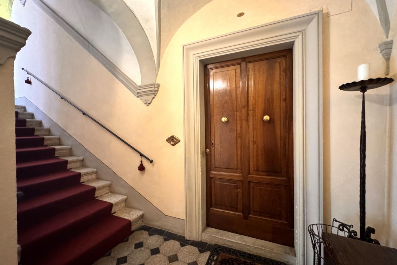Una scala con gradini rivestiti di tappeto rosso che conduce a una porta in legno con maniglie in ottone.