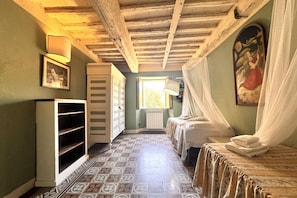 Una stanza con pavimento piastrellato, un letto a baldacchino, un termosifone, una scaffalatura e un quadro appeso al muro.