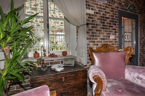 A room with a brick wall, a large window with curtains, a vintage wooden dresser, and a plush pink armchair. - Luna Ria Konuk Evi (Ayvalik)