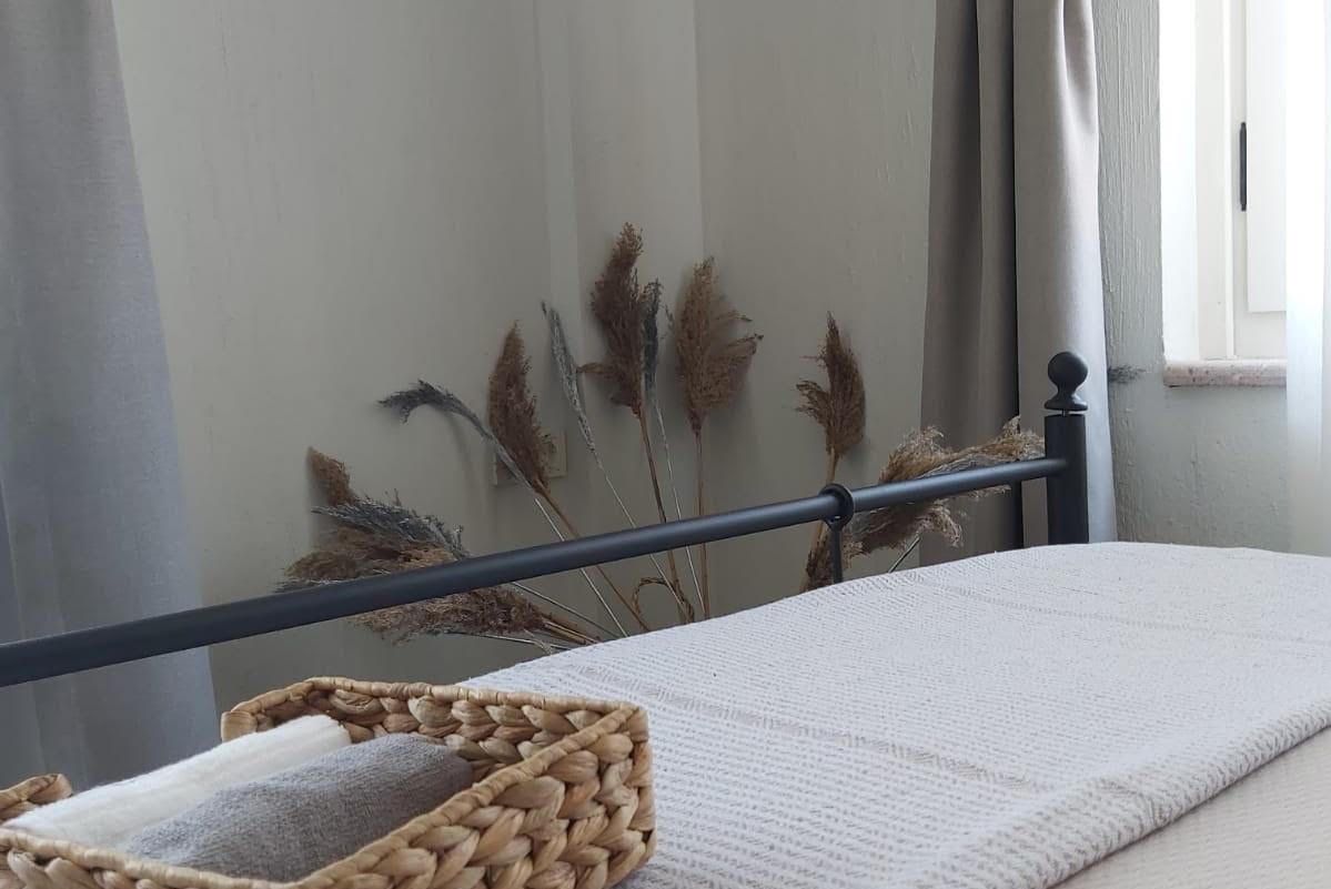 Un lit avec un drap blanc, un panier en osier et des herbes de la pampa séchées appuyées contre un mur.