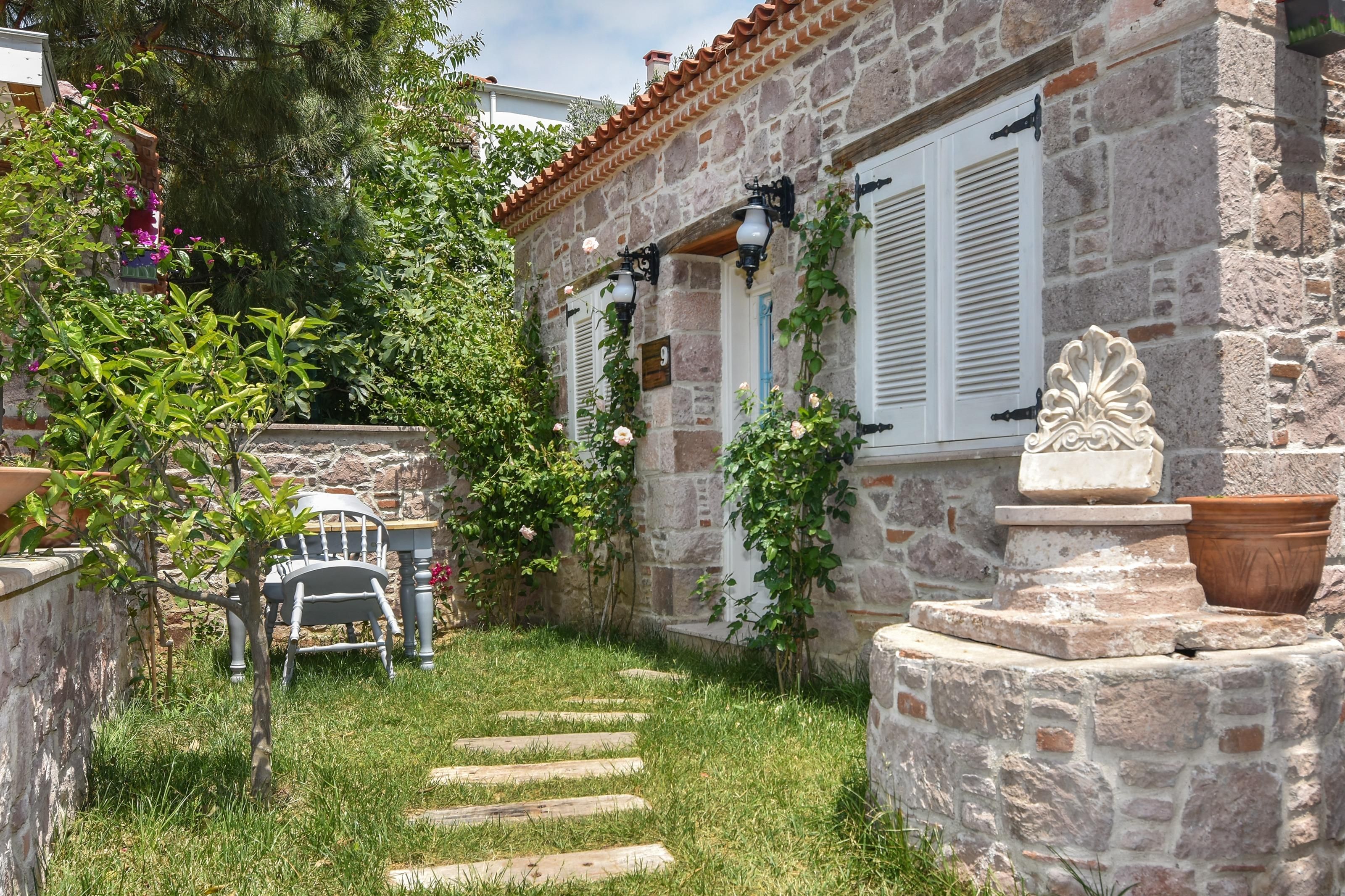 Un bâtiment en pierre doté d’un jardin, d’un banc en bois et d’un chemin menant à l’entrée.