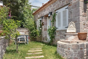 A stone building with a garden, a wooden bench, and a pathway leading to the entrance. - Luna Ria Konuk Evi (Ayvalik)