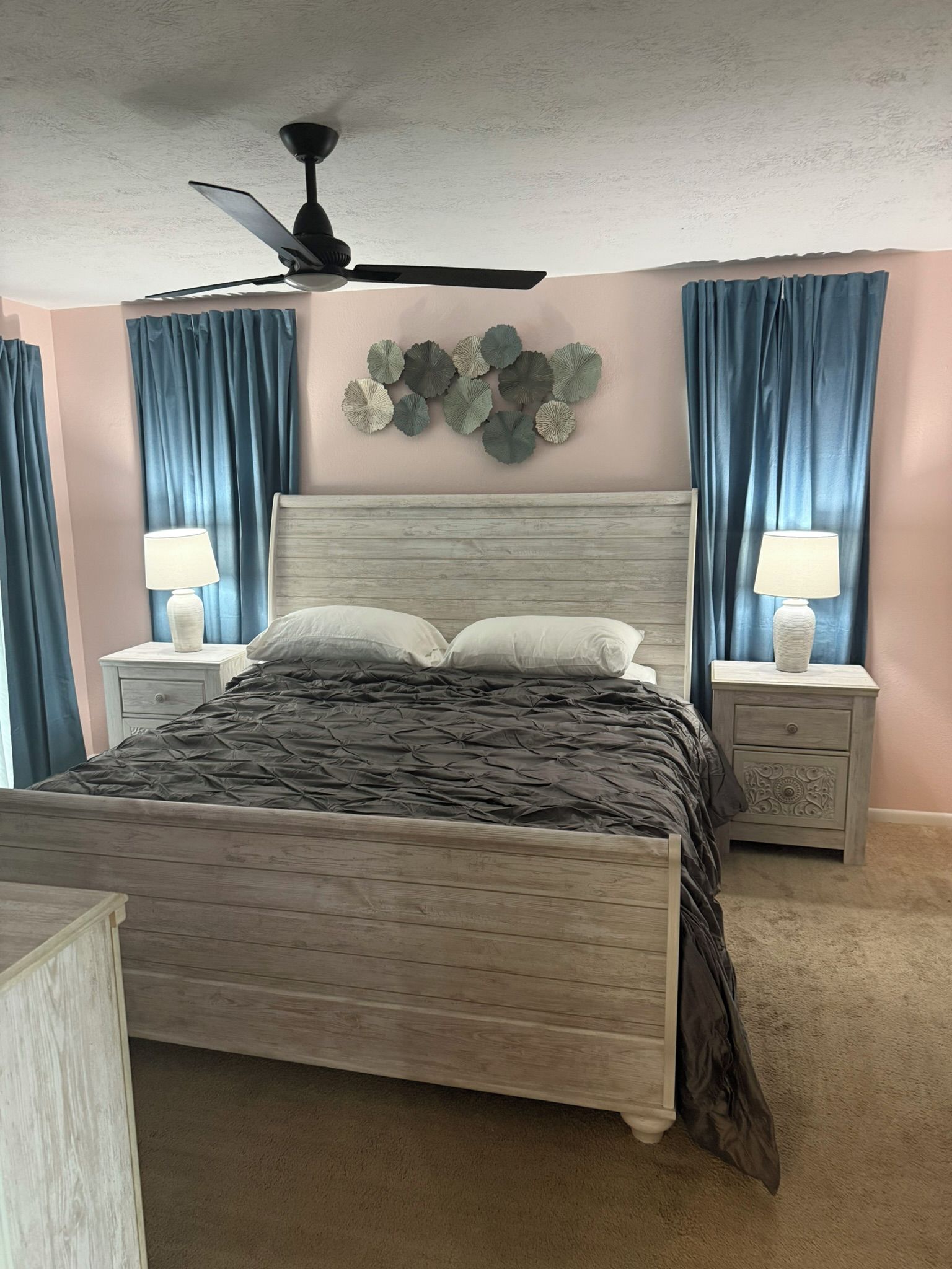 A bedroom with a bed, two nightstands, a ceiling fan, and curtains.