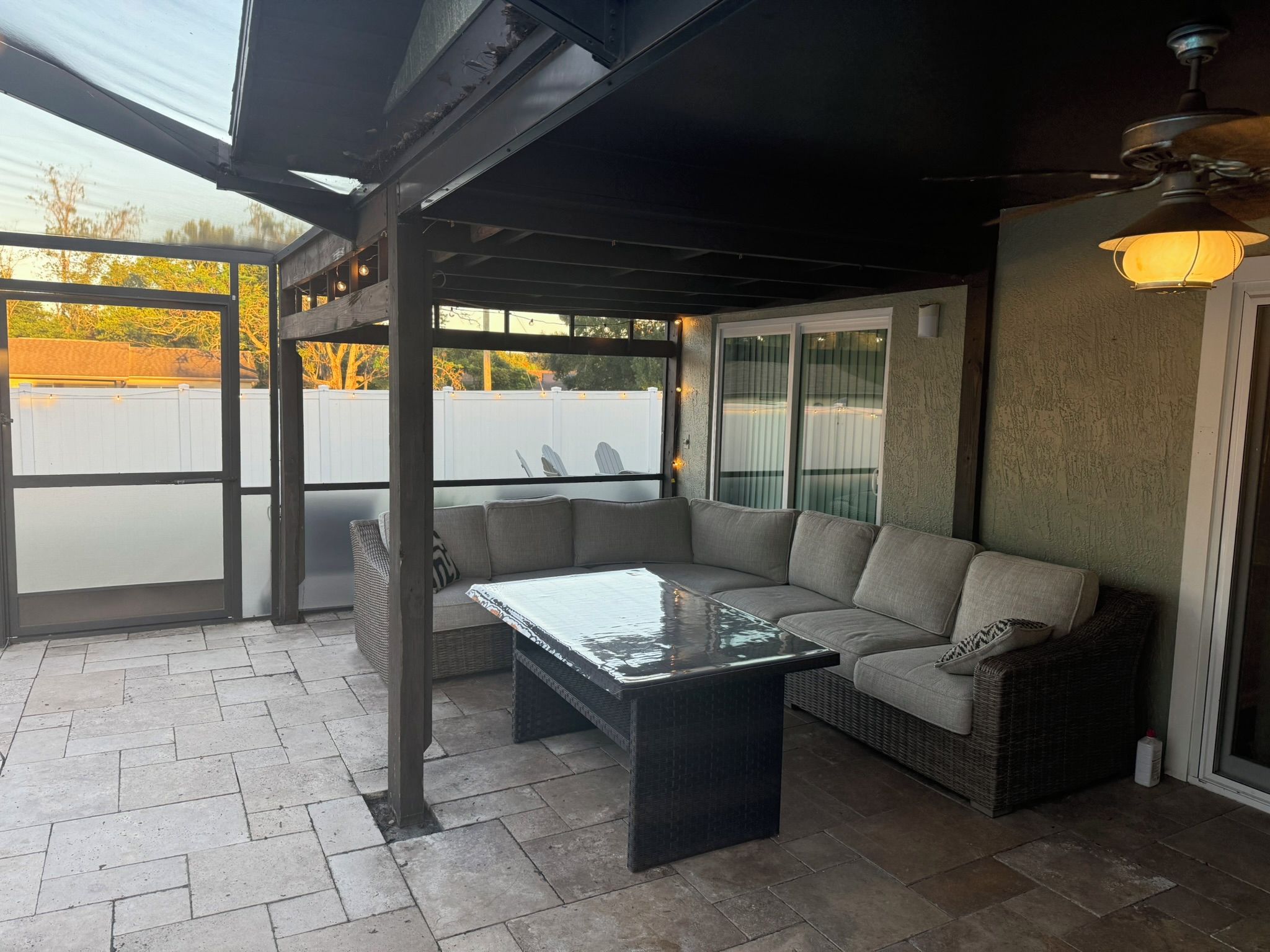 A covered patio area with a sectional sofa, a glass-top coffee table, and a wicker chair.