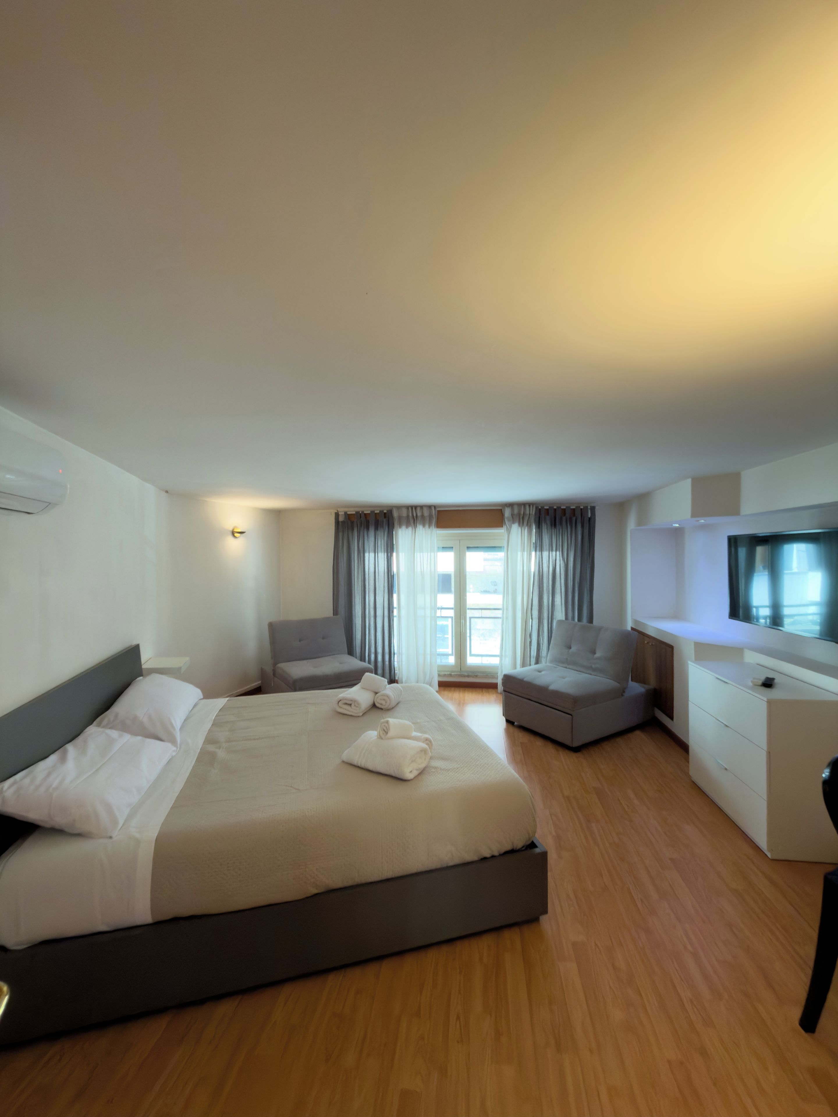 Una habitación de hotel con una cama grande, dos sillones, un televisor y un escritorio.