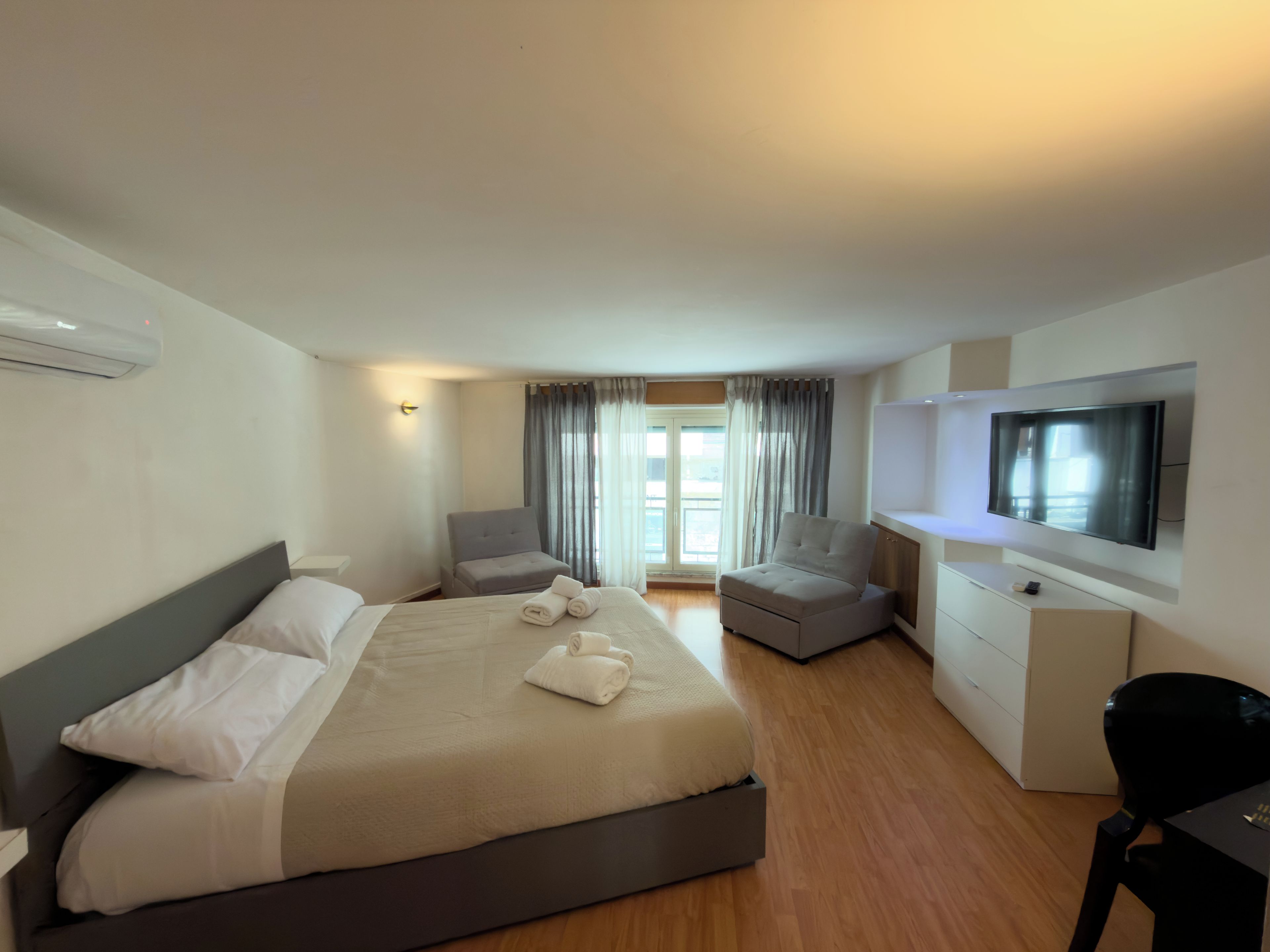 Habitación de hotel con cama, escritorio, silla, televisión y ventana con cortinas.