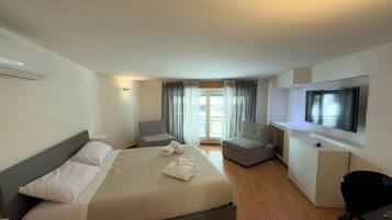 Habitación de hotel con cama, escritorio, silla, televisión y ventana con cortinas.