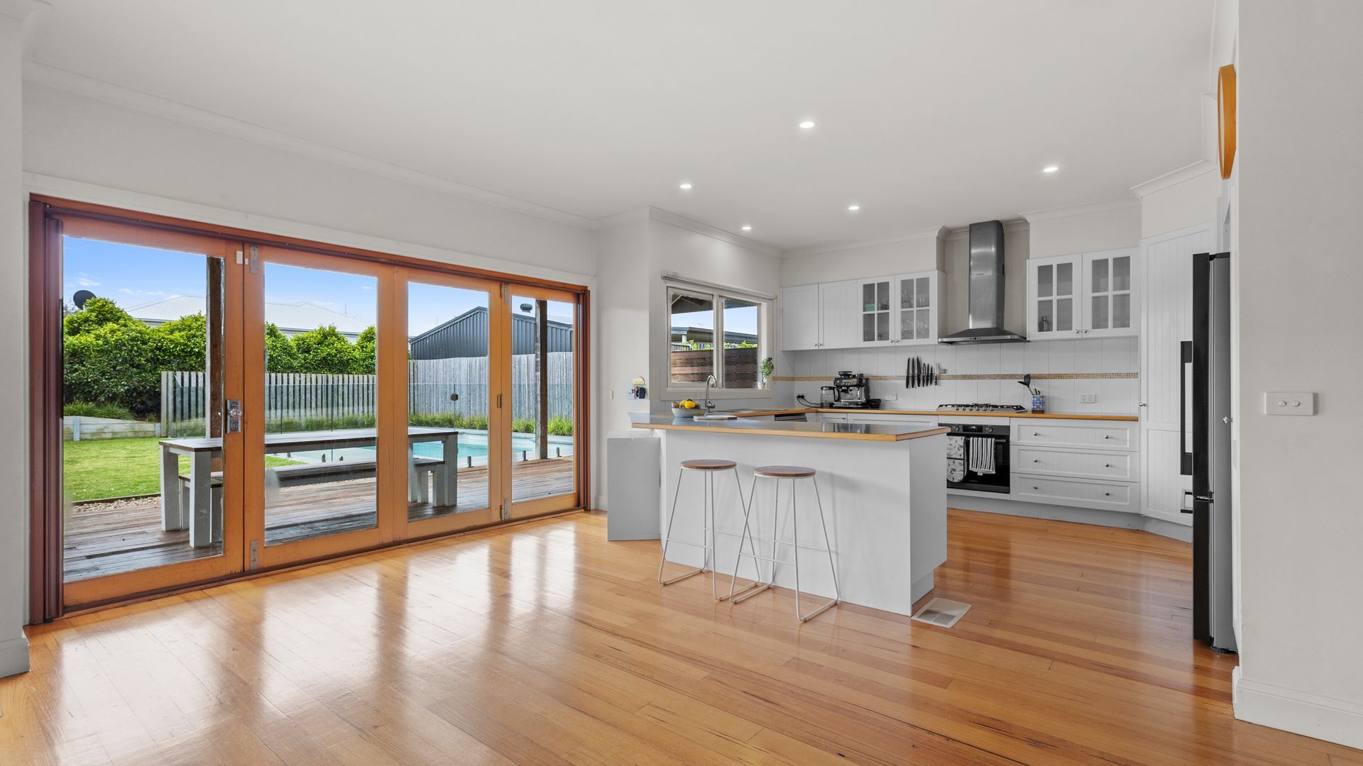 A modern kitchen with a large island, bar stools, and a sliding glass door leading to a backyard.