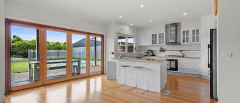 A modern kitchen with a large island, bar stools, and a sliding glass door leading to a backyard.