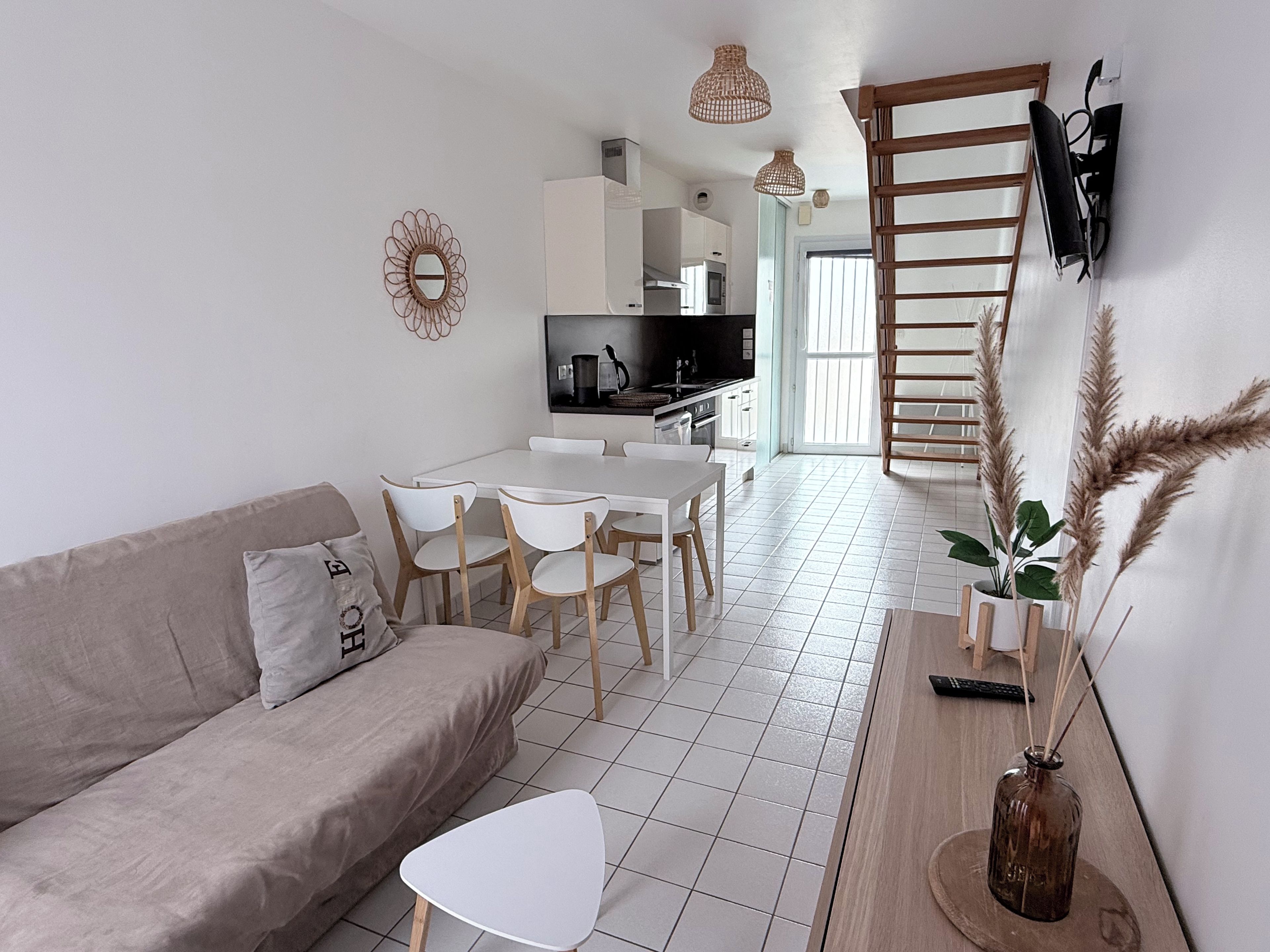 A modern living room with a sofa, dining table, chairs, and a kitchen in the background.