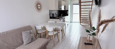 A modern living room with a sofa, dining table, chairs, and a kitchen in the background.