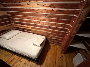 Een houten blokhut van binnen, met een bed, houten wanden en een schuin dak.