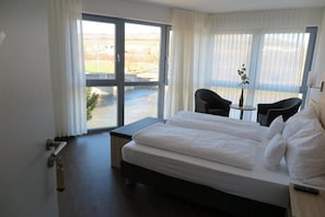 A hotel room with a large bed, a small table, two chairs, and a view through a sliding door.