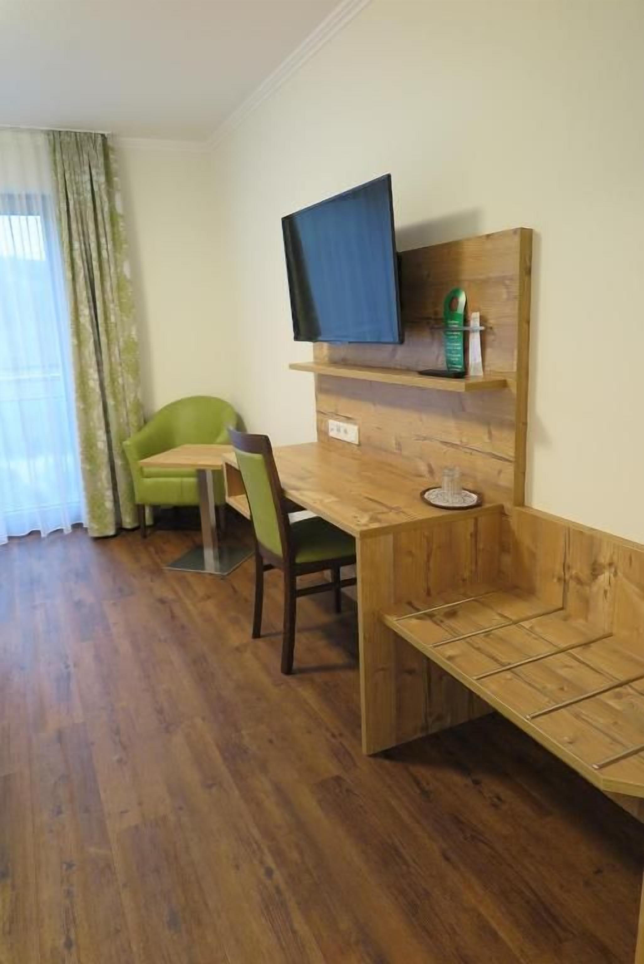 Una habitación con una mesa de madera, dos sillas, un televisor fijado en un estante de madera y una ventana con cortinas.