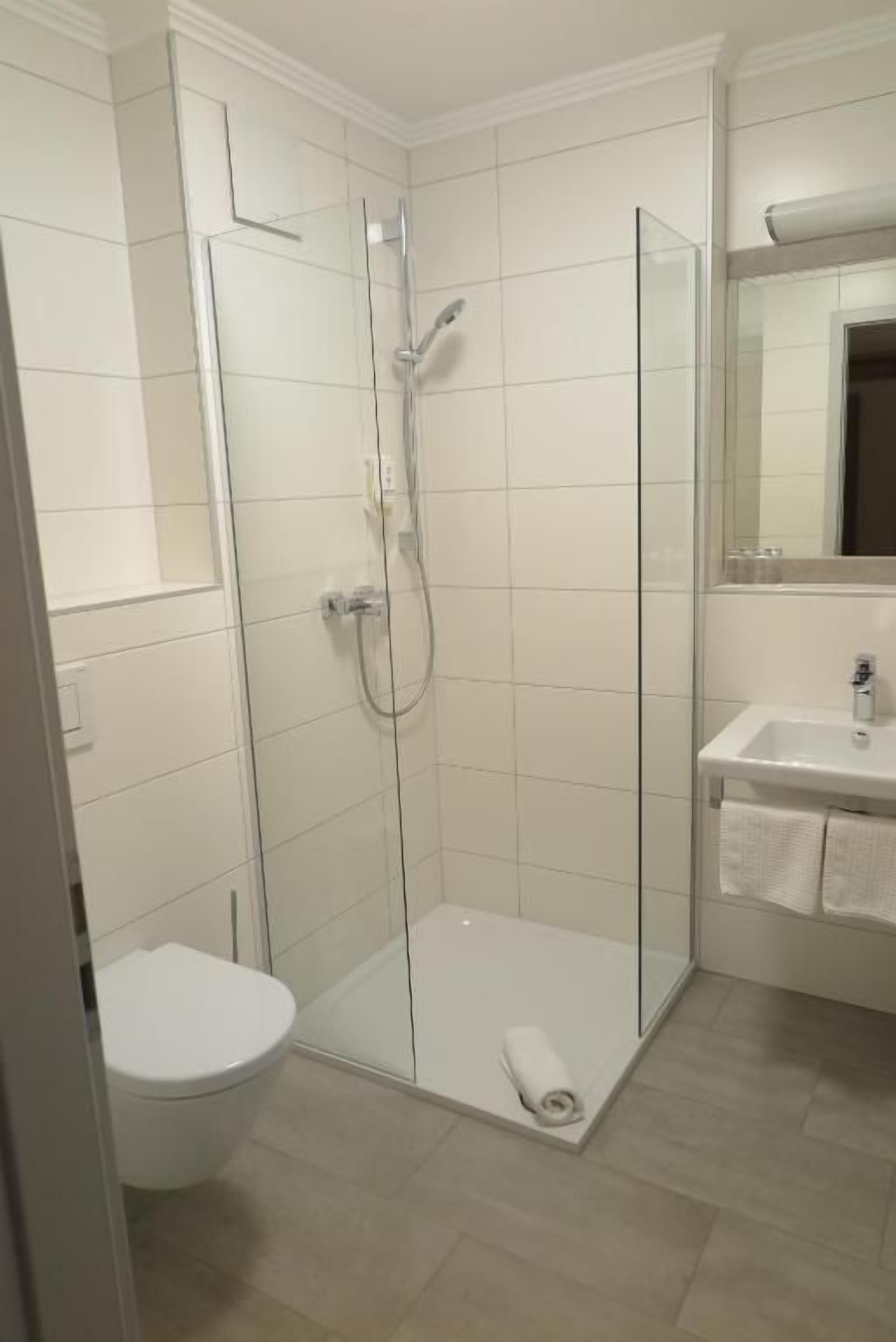 Kylpyhuone, jossa on lasiseinällä varustettu suihku, wc ja pesuallas, jonka päällä on pyyhe.
