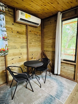Un intérieur en bois avec une table et des chaises, un appareil de climatisation et une fenêtre donnant sur un paysage verdoyant.