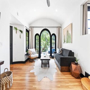 A spacious living room with a cowhide rug, a sofa, a coffee table, and a view through arched windows. - South Park Spanish Stunner Renovated & Central (San Diego)