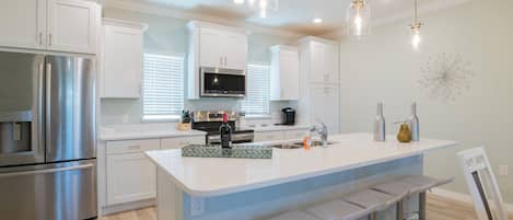 A modern kitchen with white cabinetry, stainless steel appliances, a central island with bar stools, and pendant lighting.