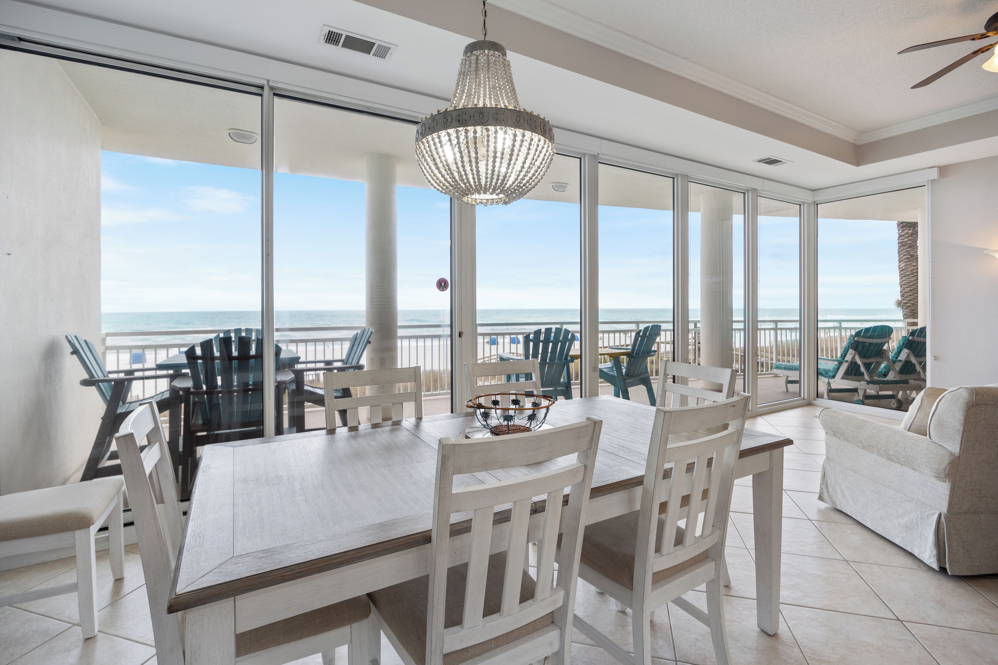 A dining area with a view of the ocean, a chandelier, and a balcony with chairs.