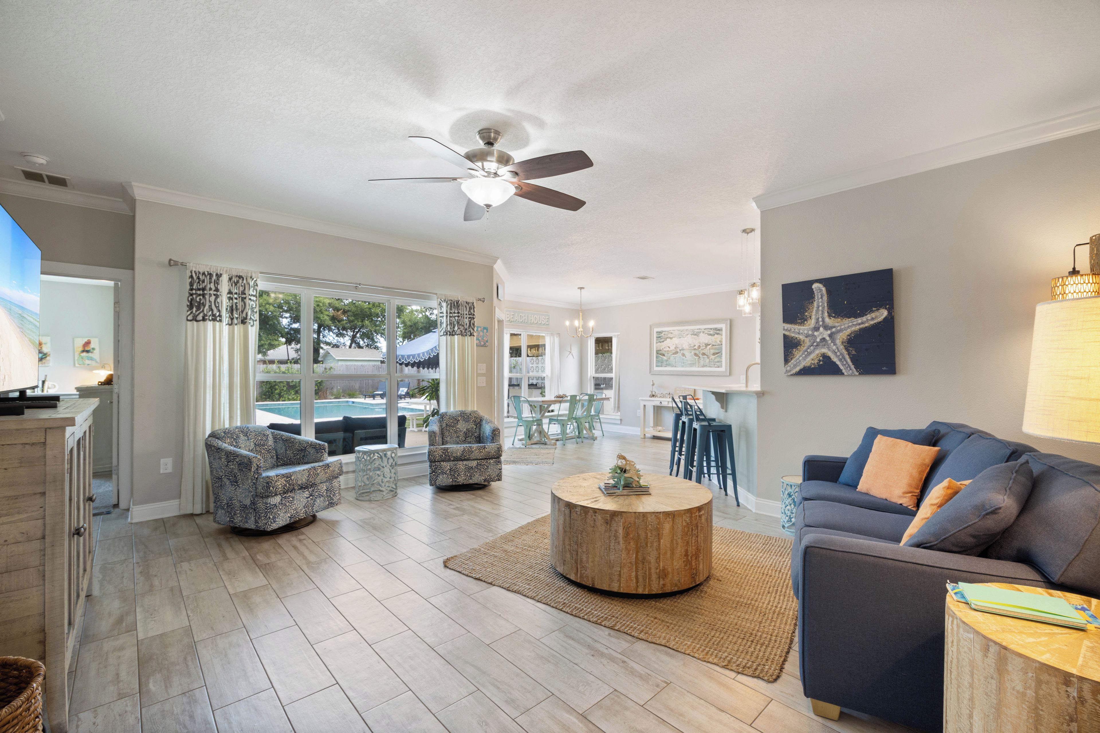 A spacious living area with a ceiling fan, a round wooden coffee table, and a blue sofa with orange cushions.