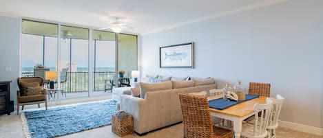 A living room with a sofa, dining table, chairs, and a large window with a view.