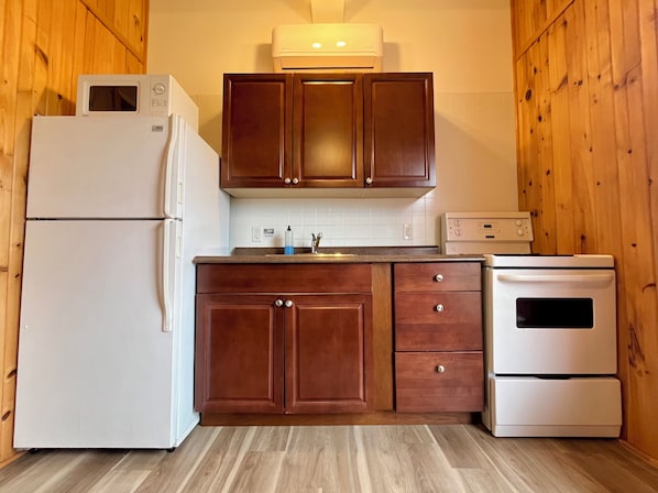 Une cuisine avec des meubles de rangement en bois, un réfrigérateur blanc, un four à micro-ondes, un évier et une cuisinière.