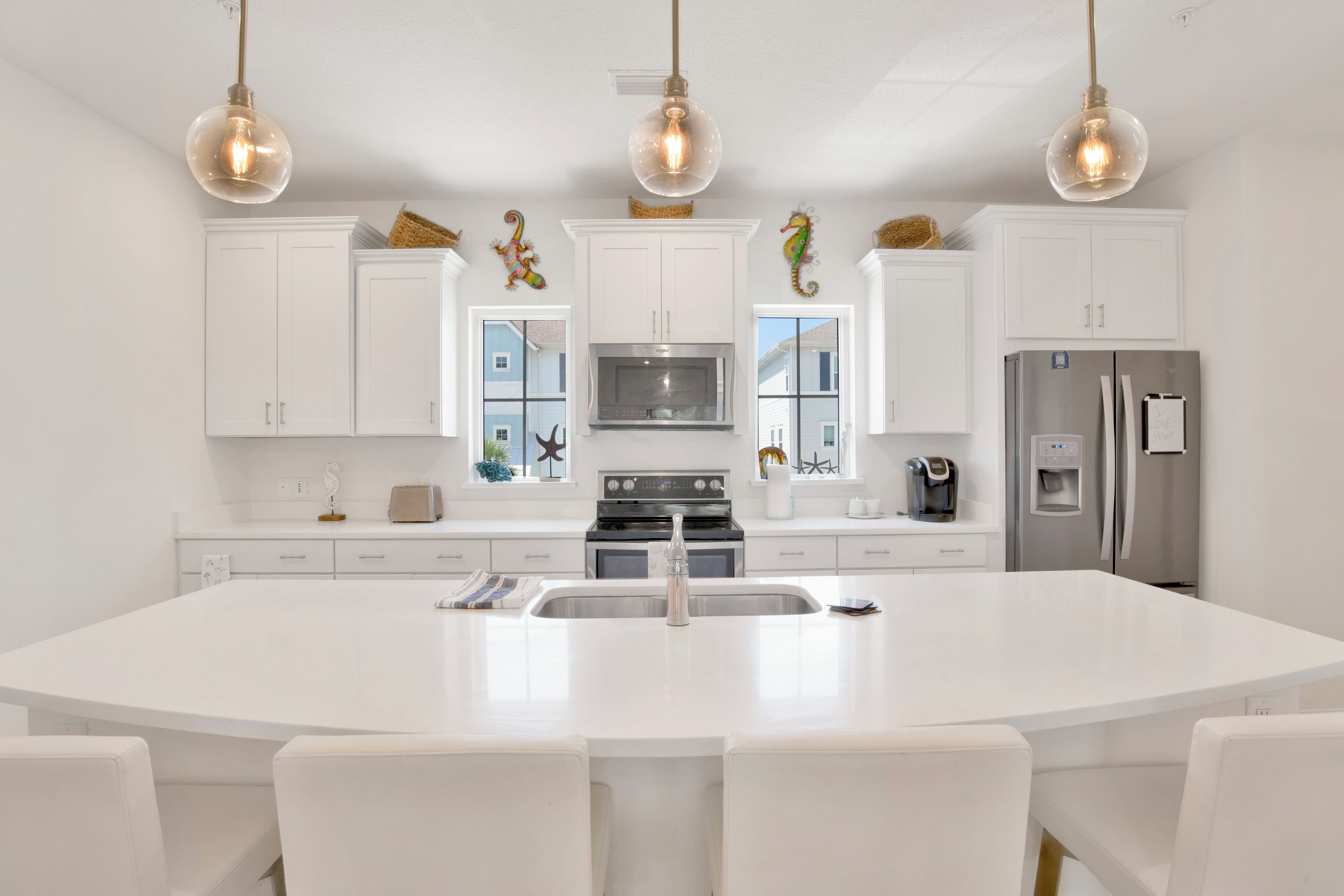 A modern kitchen with white cabinetry, a large island with seating, stainless steel appliances, and decorative wall art.