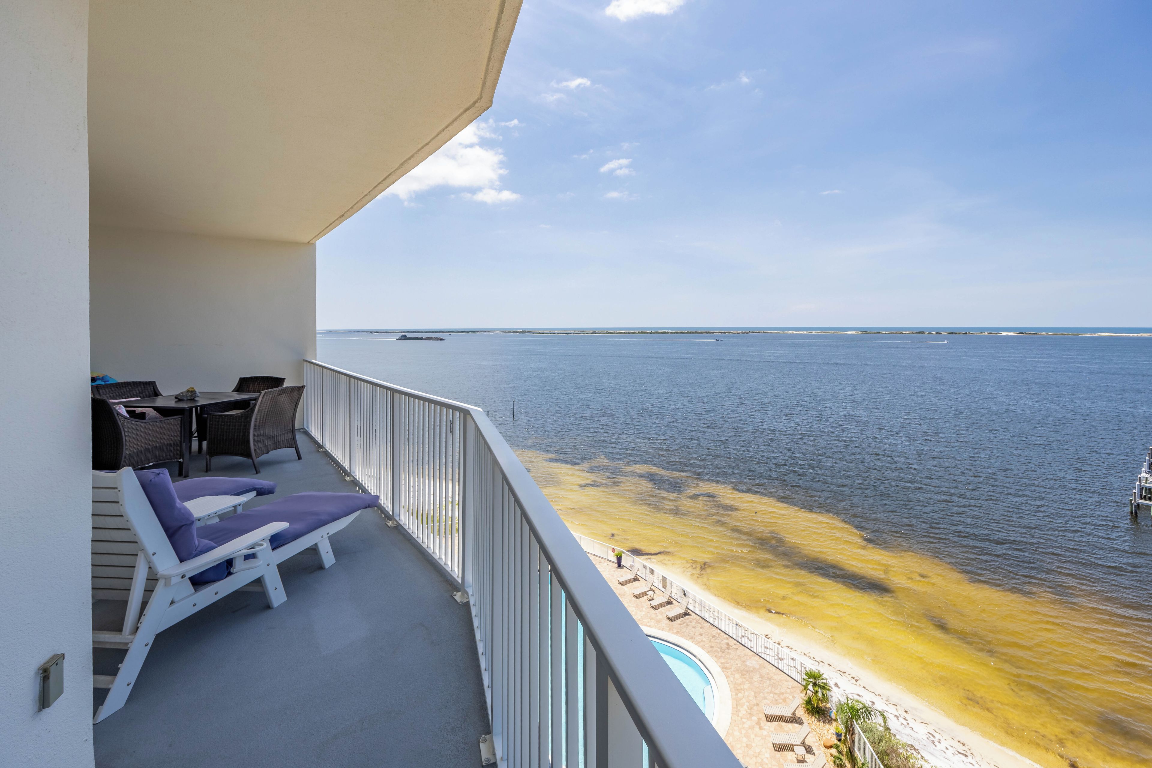 A balcony with lounge chairs, a table, and a view of the sea.