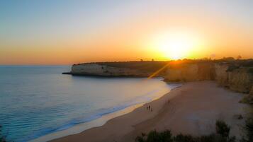A beach with a cliff, calm sea, and a sunset.