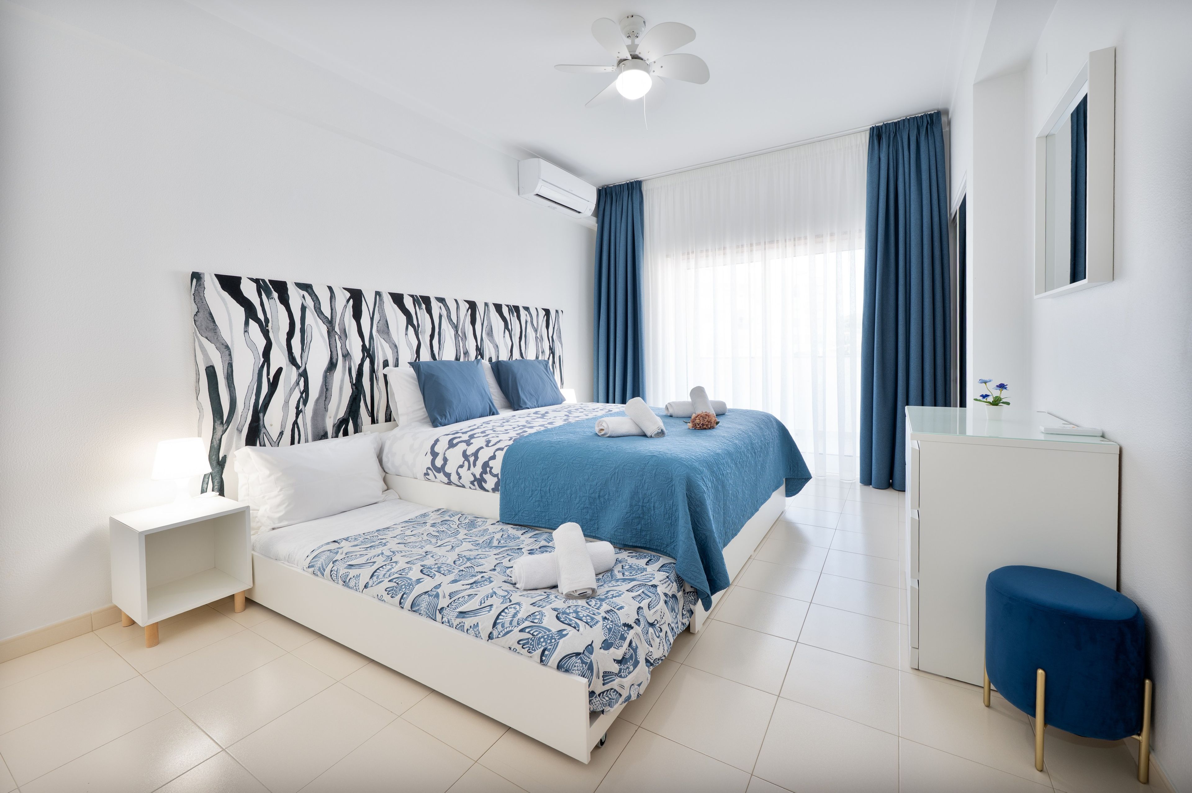 A modern hotel room with a bed, bedside table, and a desk with a chair.