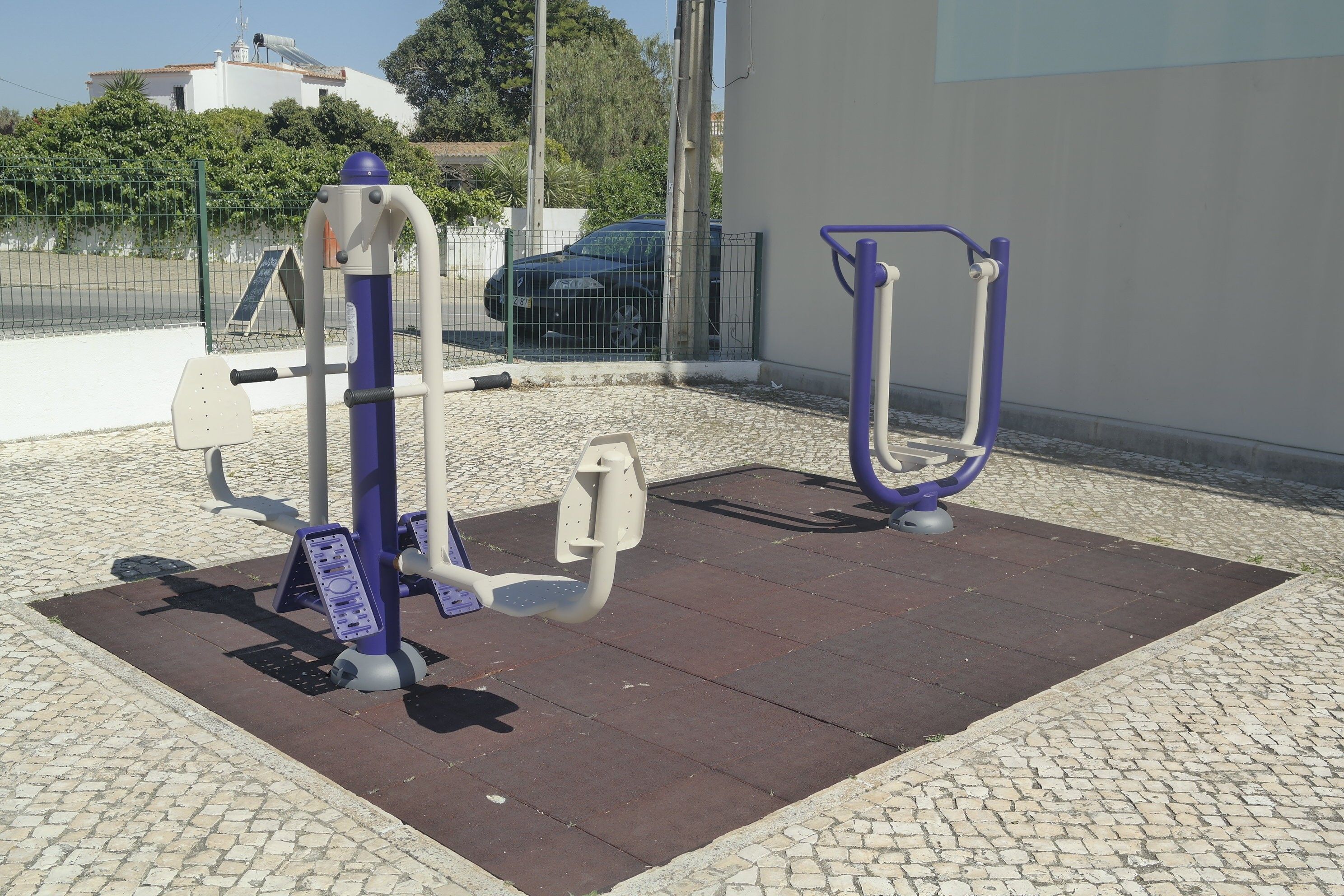 Outdoor exercise equipment on a paved area with a building in the background.