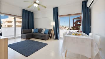A modern living room with a sectional sofa, a dining table set for breakfast, and a large window with a view of buildings.