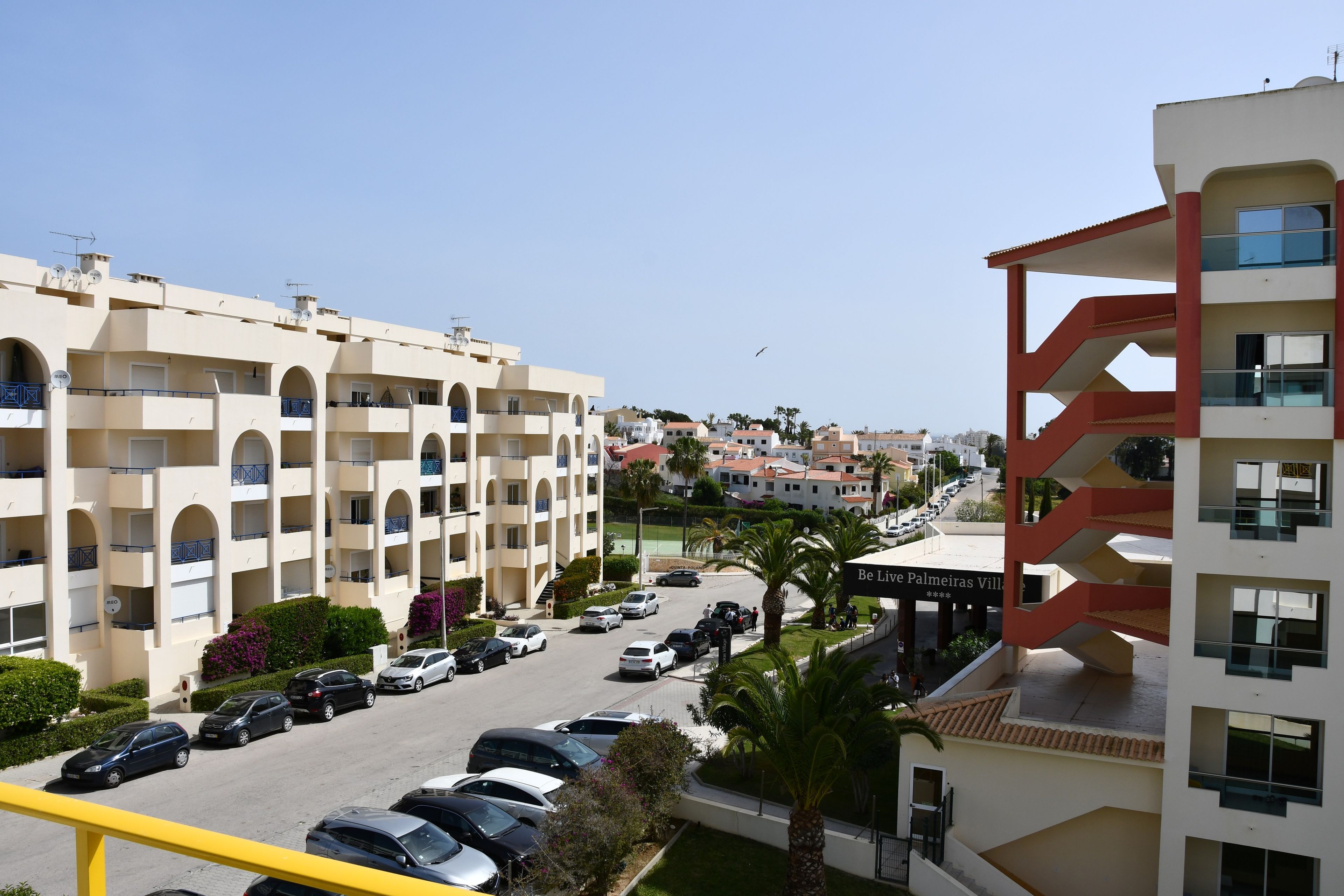 A multi-story residential building with balconies, a parking area, and a clear view of the surrounding neighborhood.