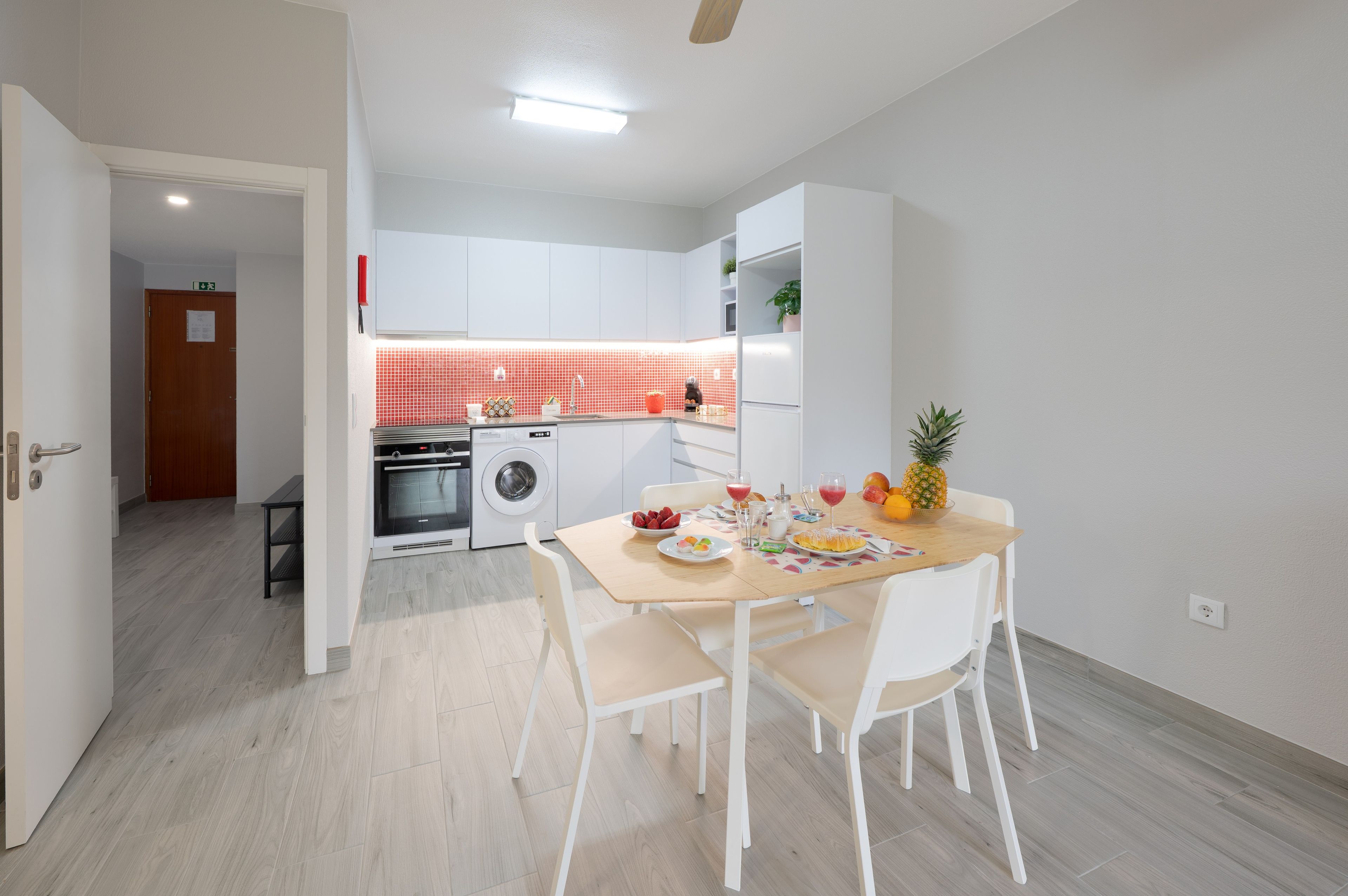 A modern kitchen with white cabinets, a red backsplash, and a dining area with a table set for two.