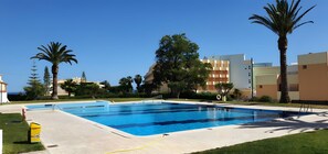 A swimming pool with a clear blue water surface, surrounded by a paved deck and a grassy area. - Holiday Home 'Casa Morango - Senhora Da Rocha' with Sea View, Wi-Fi and Air Conditioning (Porches)