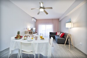 Ein modernes Wohnzimmer mit Essbereich, Deckenventilator, Sofa, Lampe und Fernseher.