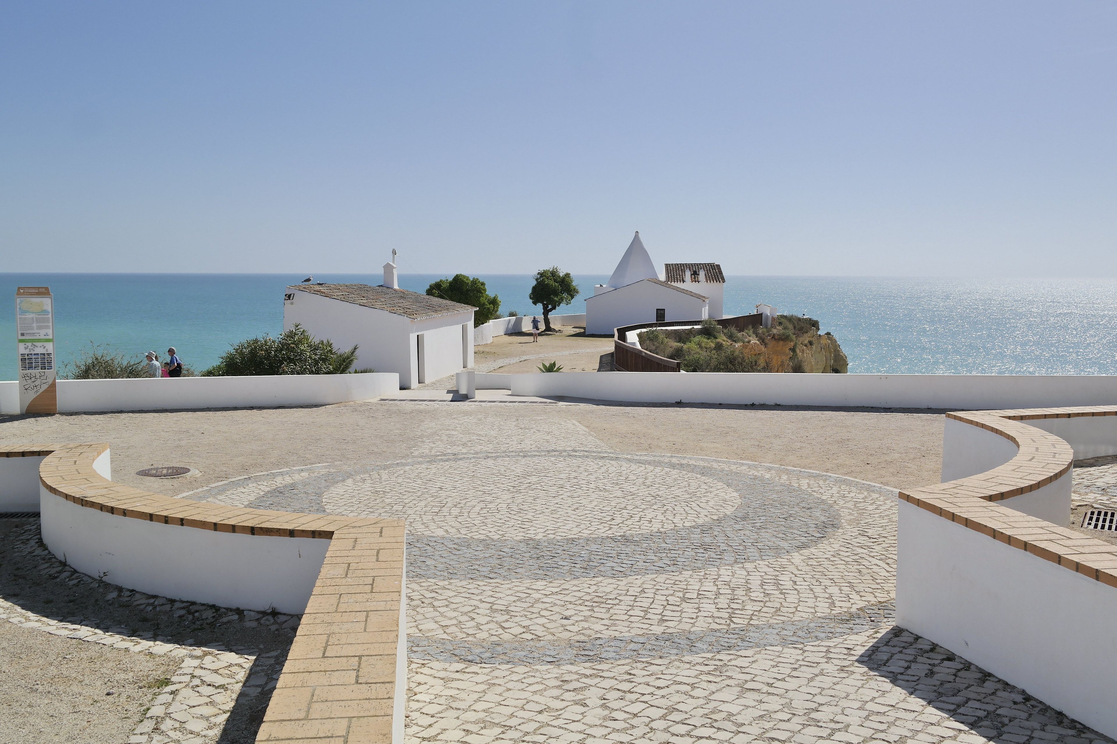 Un edificio costero con un patio empedrado, paredes blancas y vistas al mar.