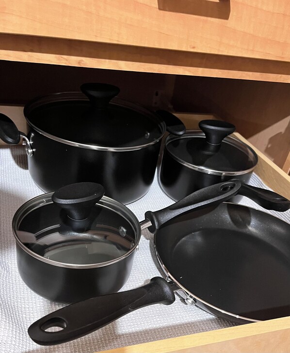 Un cajón de cocina con utensilios de cocina negros, incluyendo ollas, sartenes y una sartén.