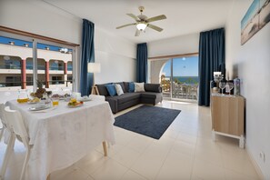 A modern living room with a sofa, dining table, and a balcony with a view. - Holiday Home 'Casa Azul 1 - Senhora Da Rocha' with Sea View, Wi-Fi and Air Conditioning (Porches)
