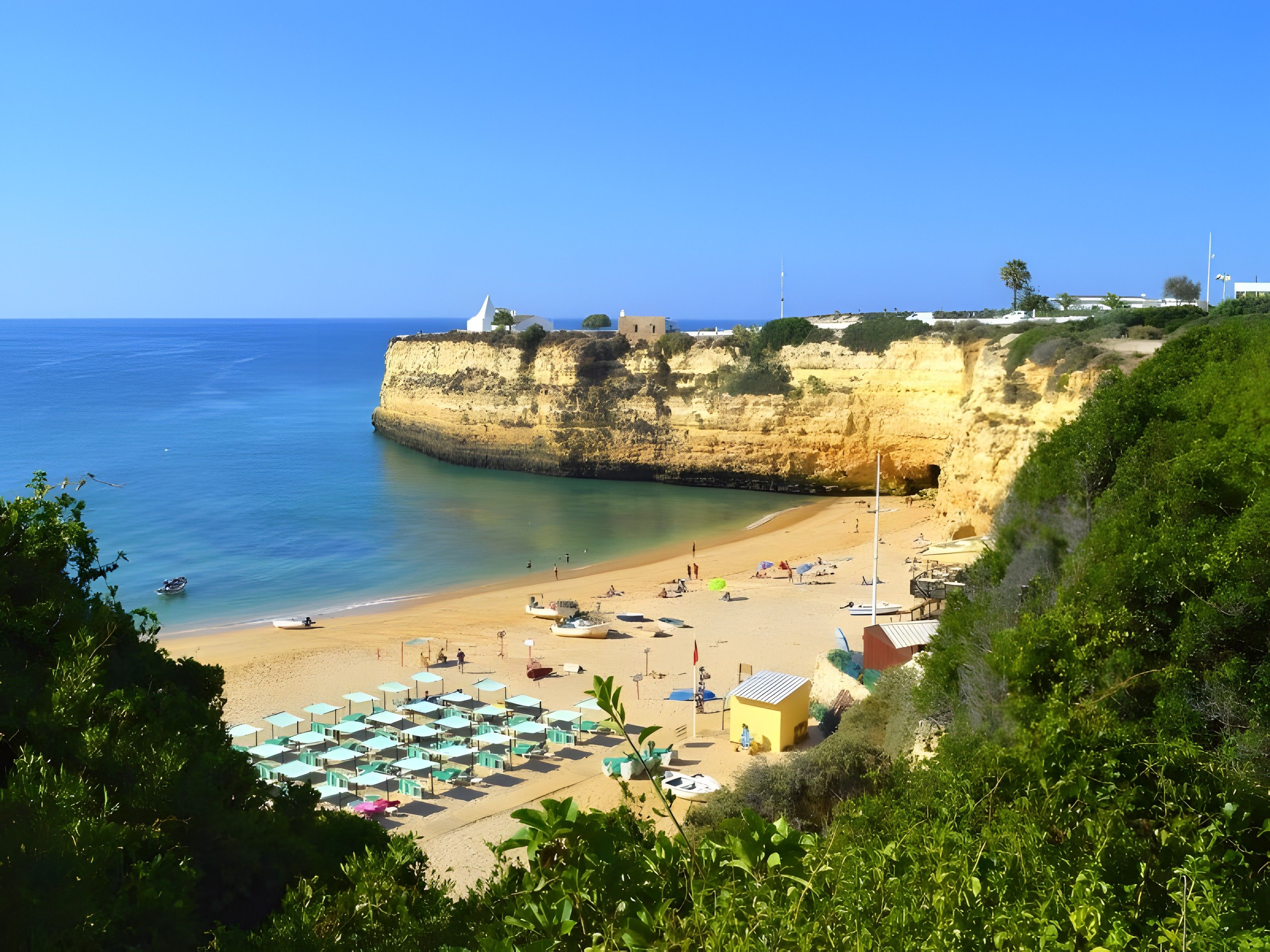 A coastal beach with a cliff, beach umbrellas, and a small building.