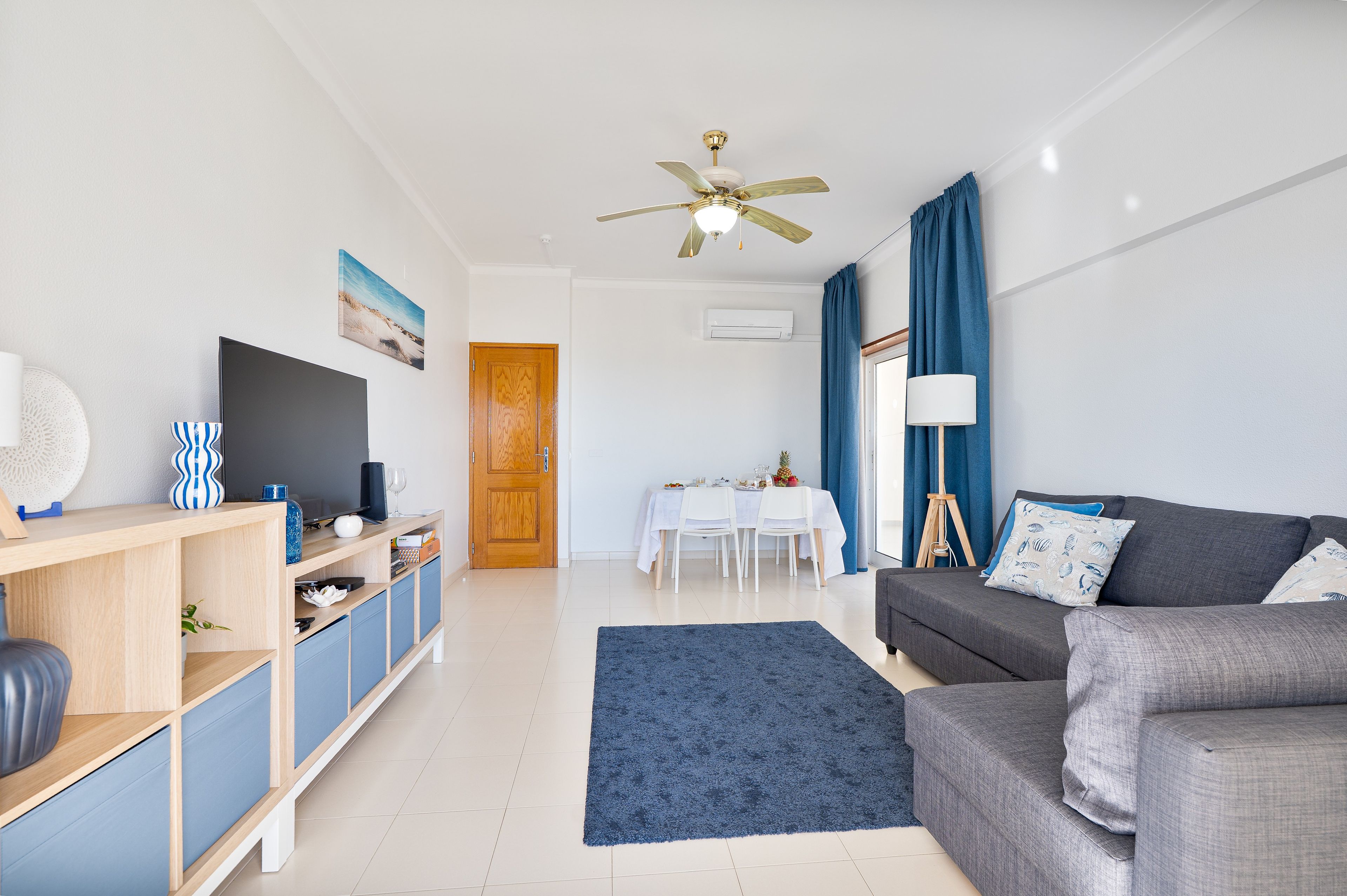 A modern living room with a grey sofa, a blue rug, a wooden cabinet, and a dining area with a table and chairs.