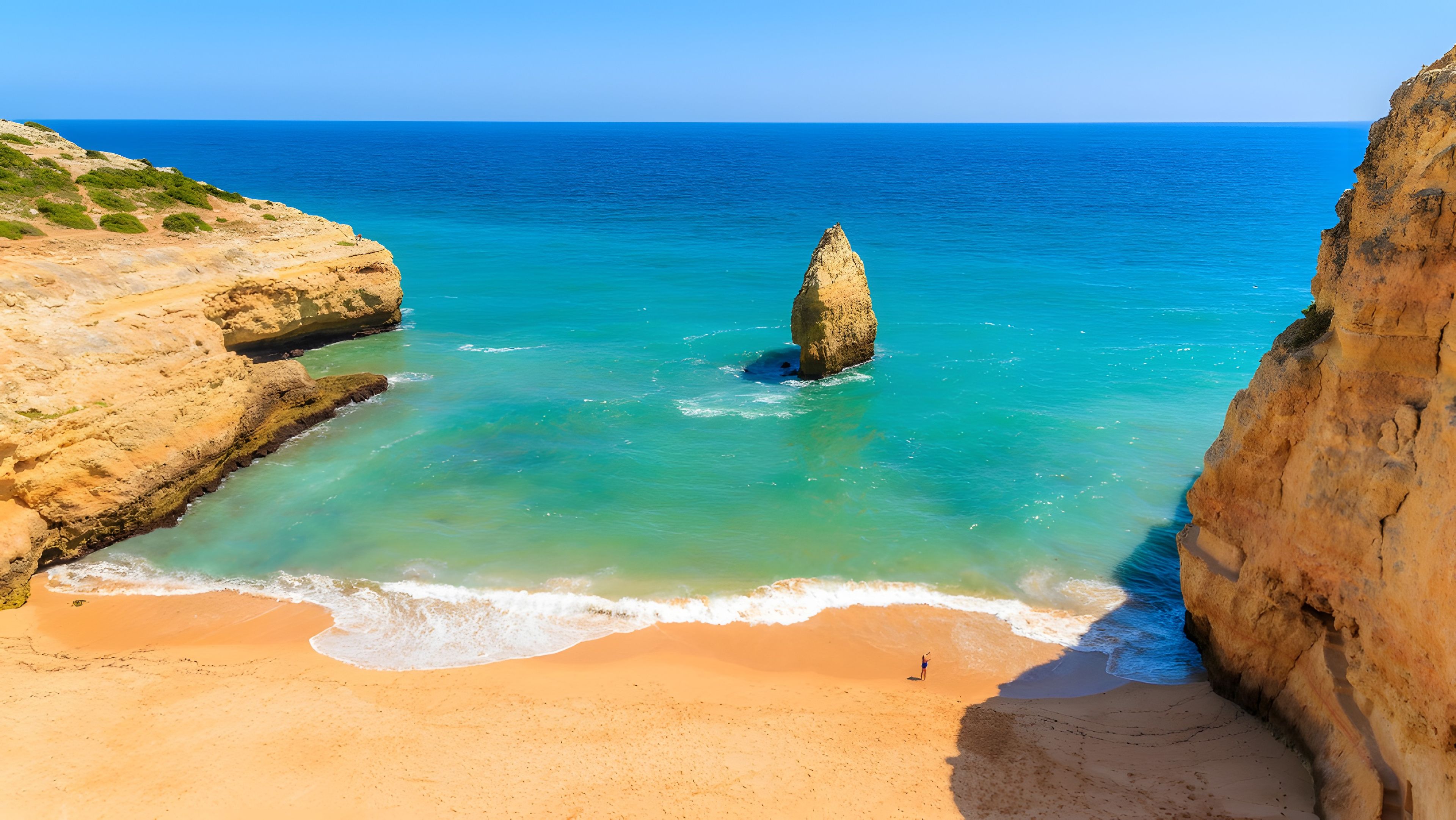 Un paisaje costero con una destacada formación rocosa en el agua, una playa arenosa y acantilados rocosos.