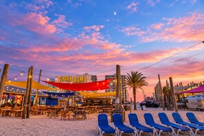 A beachside restaurant with outdoor seating, a sign reading 'FLORA-BAMA', and a sunset sky. - La Piscina Luxury Retreat with Private Heated Pool, Spa and Putting Green (Pensacola)