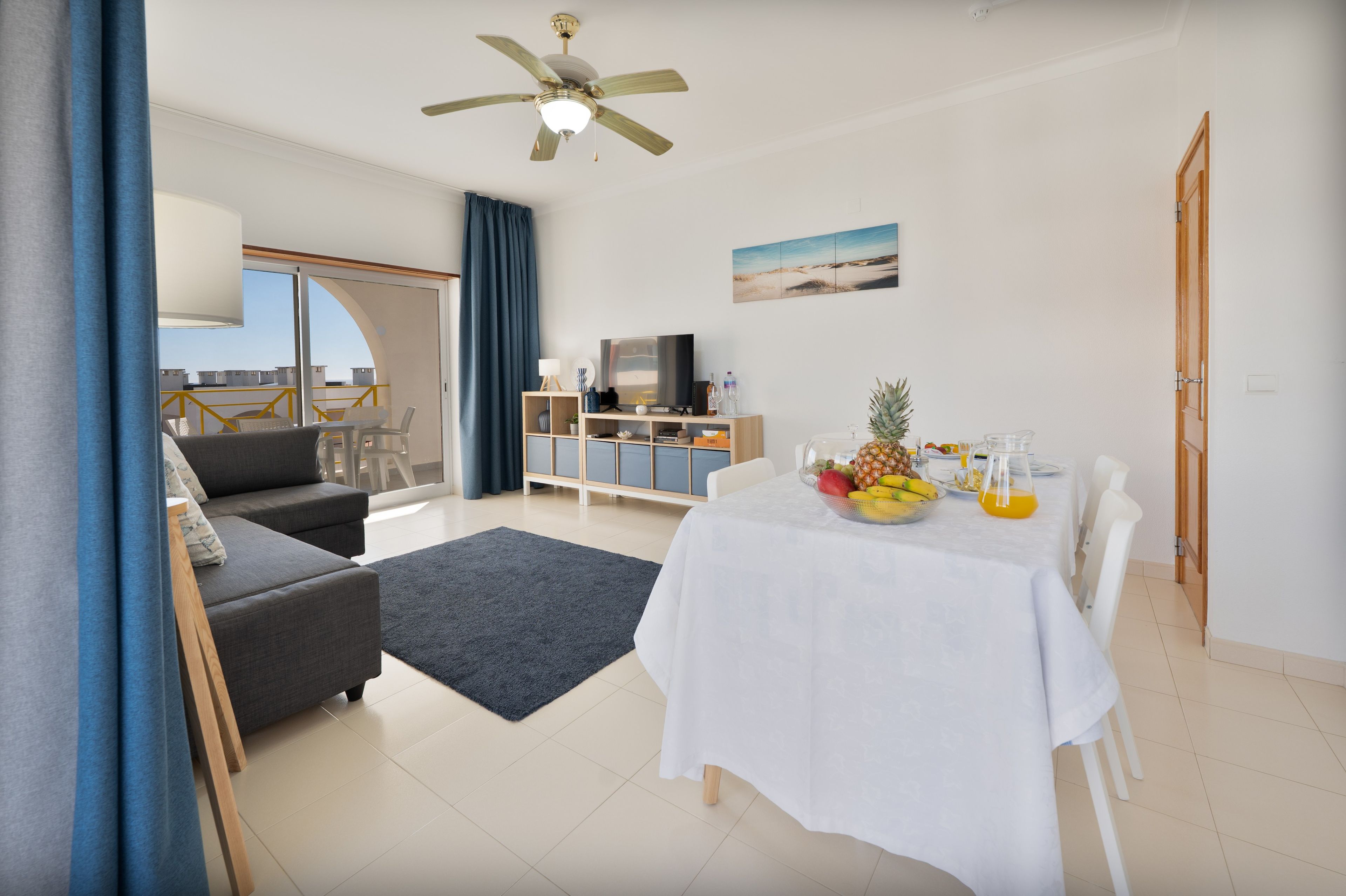 Una sala de estar moderna con un sofá, una mesa de comedor con fruta, un televisor y un ventilador de techo.