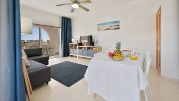 Una sala de estar moderna con un sofá, una mesa de comedor con fruta, un televisor y un ventilador de techo.